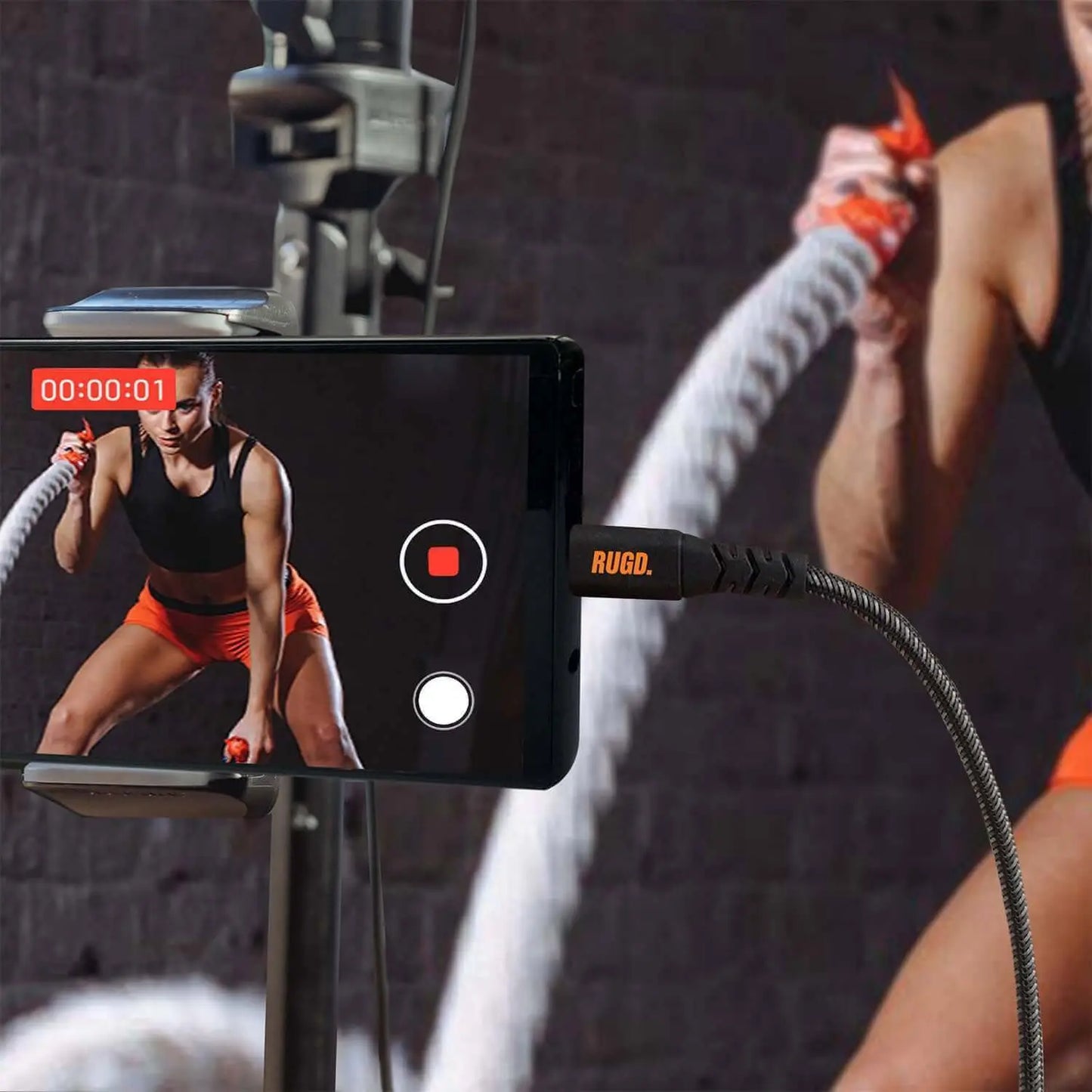 Athlete recording battle ropes workout with RUGD USB-C charging cable connected to smartphone.
