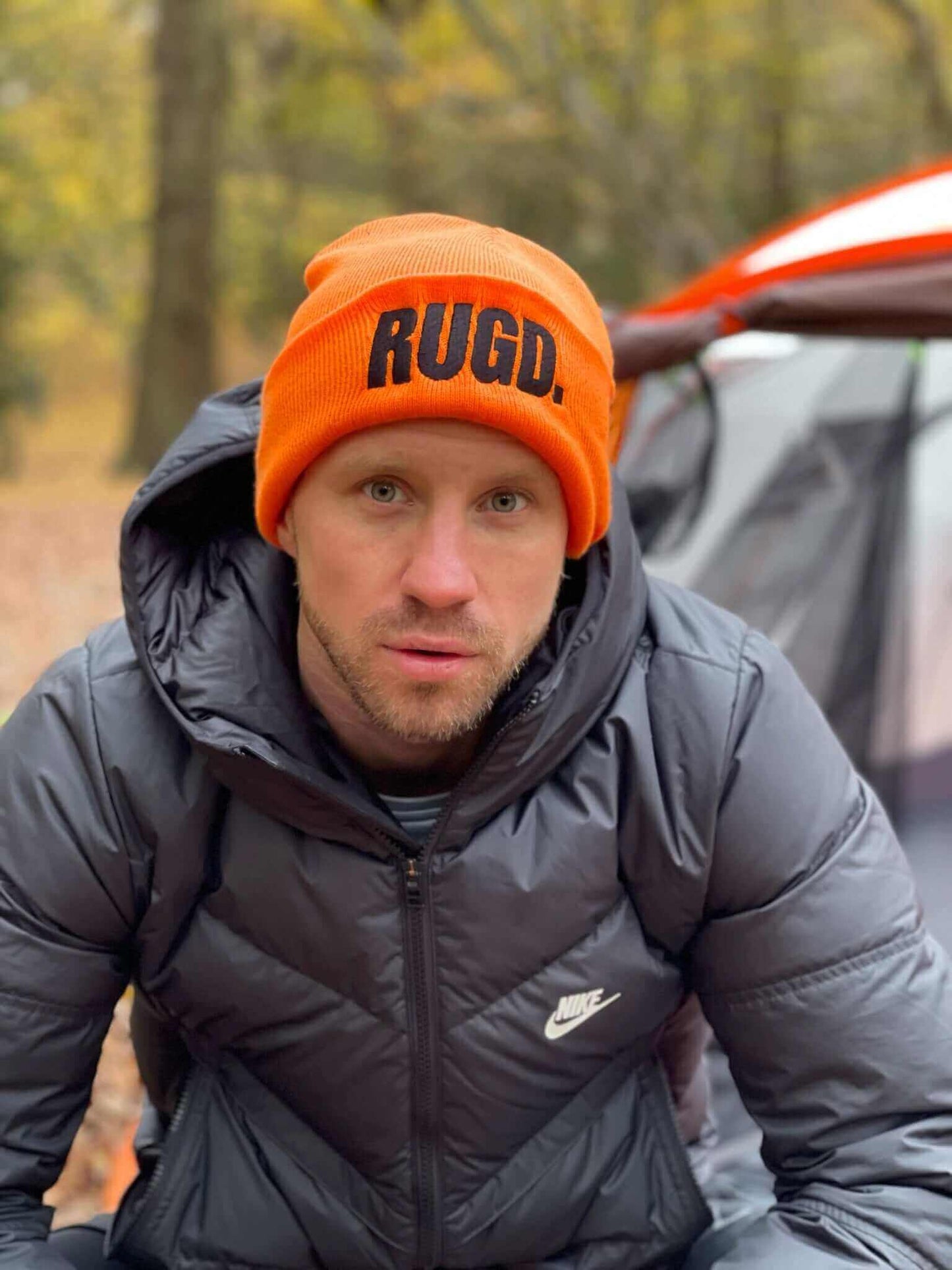 Man wearing RUGD. unisex orange beanie hat in outdoor setting.