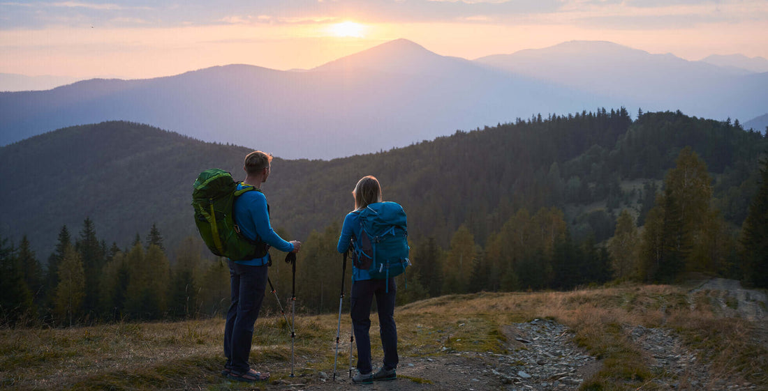 Hikers with backpacks enjoy a scenic mountain view at sunset, emphasizing safety and preparedness for outdoor adventures.