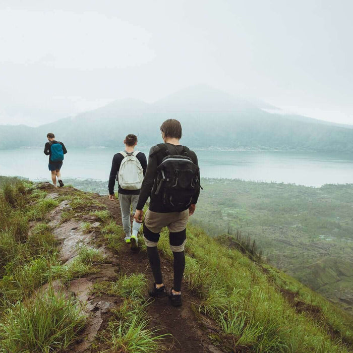 Hikers walking along a lush green mountain trail overlooking a serene lake on a foggy day