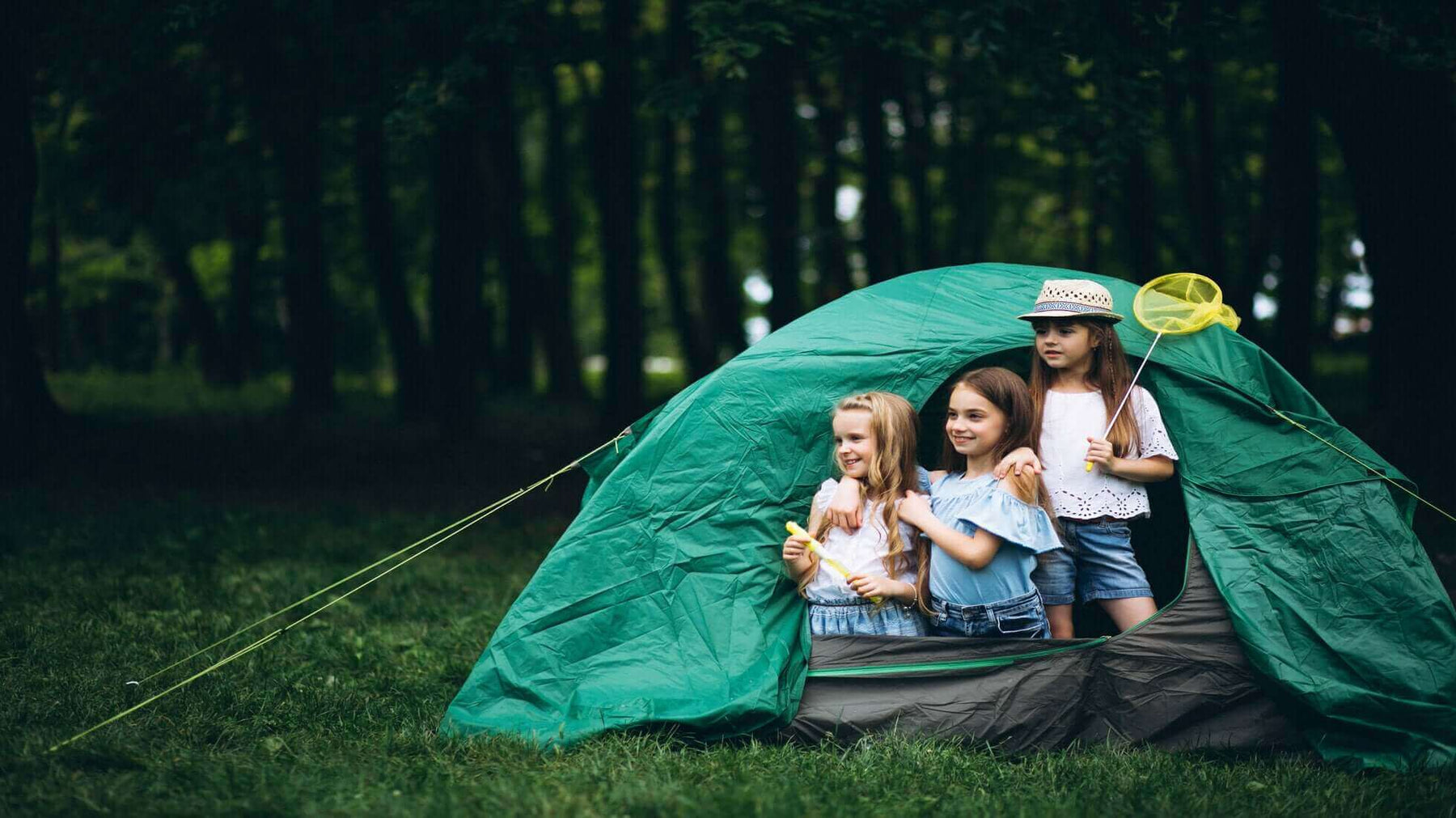 Three kids enjoying a camping trip inside a green tent, showcasing the fun of camping with kids.