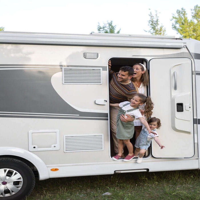 Family enjoying an RV trip, stepping out of their motorhome parked in a scenic natural setting with trees.