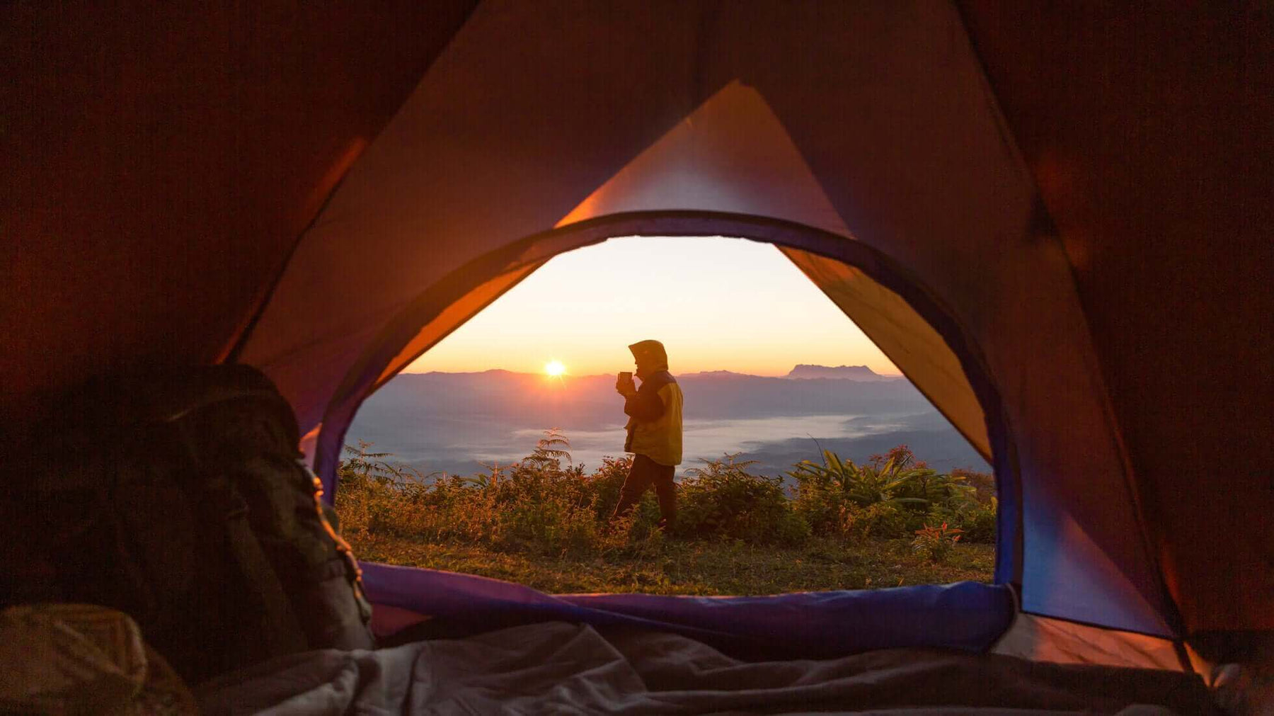 View from inside a tent of a person enjoying a sunrise on an eco camping trip in the UK.