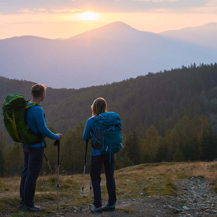 Two hikers stand on a mountain trail at sunrise, showcasing the beauty and safety of an outdoor adventure.