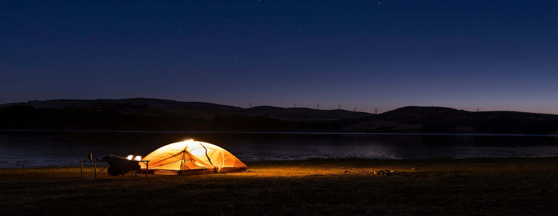 Illuminated tent by a lake under a starry night sky, perfect setting for a peaceful night-time camping adventure.