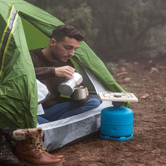 Solo camper pouring drink next to green tent and camping stove in the UK wilderness