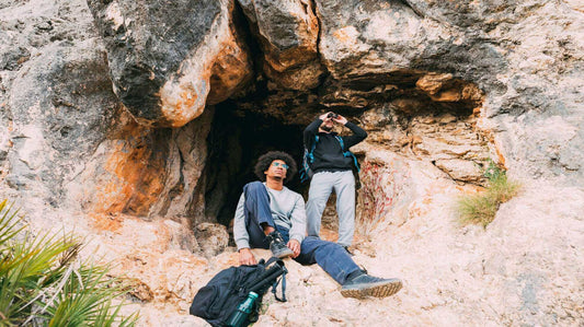 Two cavers resting outside a rocky cave entrance on a caving trip in the UK.