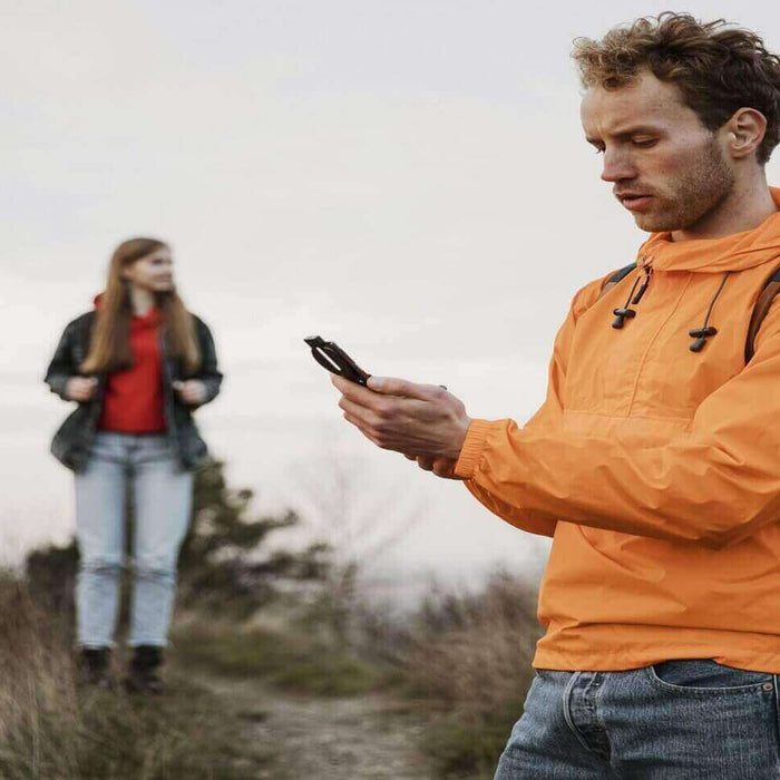 Camper using a smartphone app for navigation during a hike in the wilderness with a companion in the background.