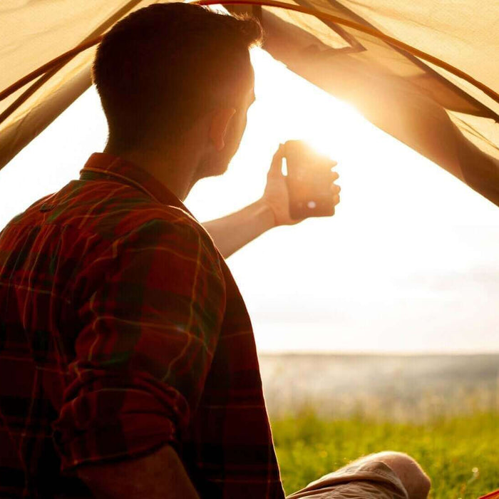 Camper enjoying sunrise from tent, staying cool with summer camping hacks.