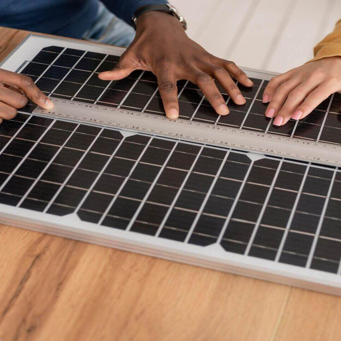 Hands measuring solar panel dimensions on a wooden table