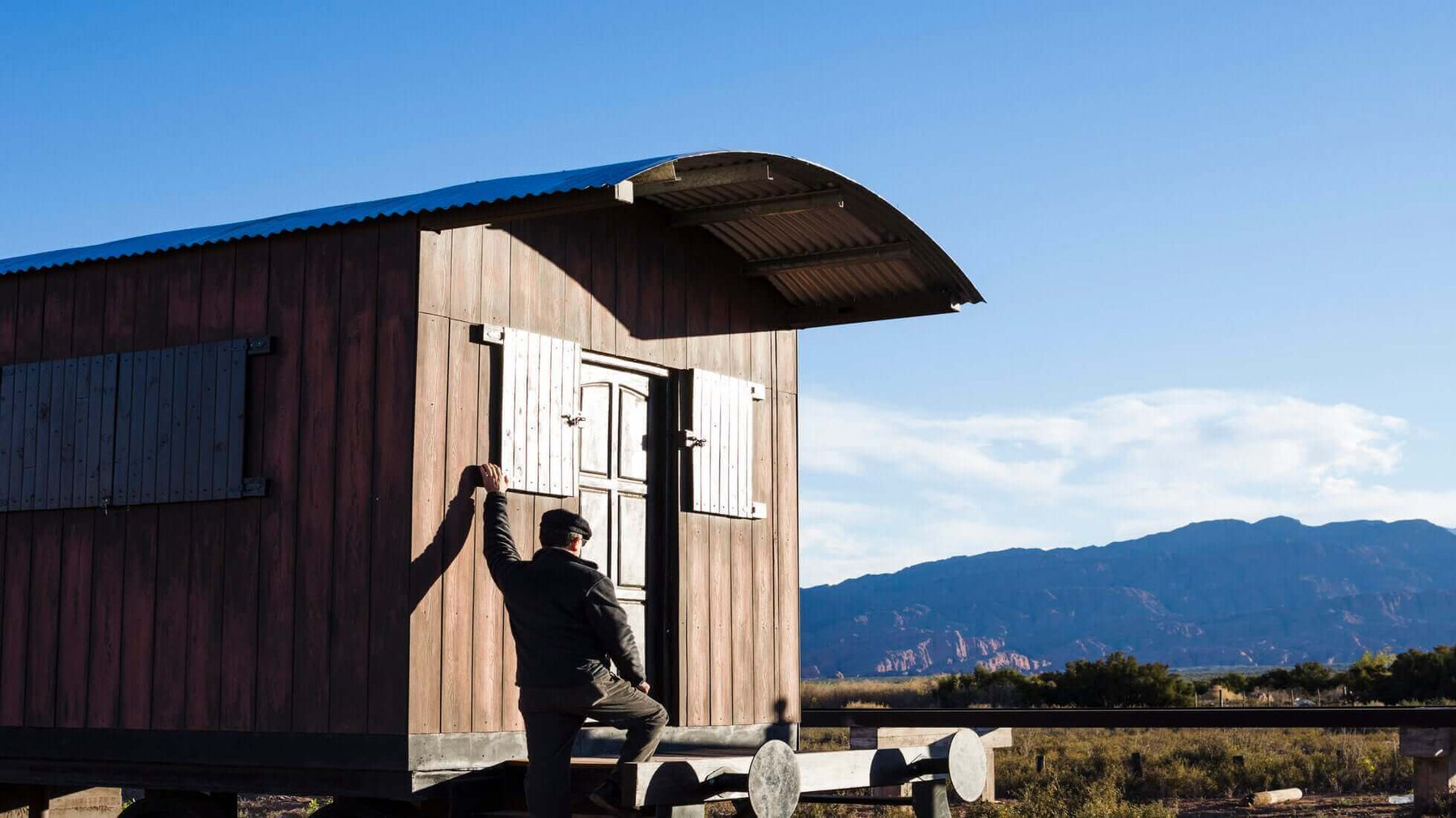 Man entering an off-grid cabin in a remote location with mountain views, showcasing sustainable living and independent lifestyle.