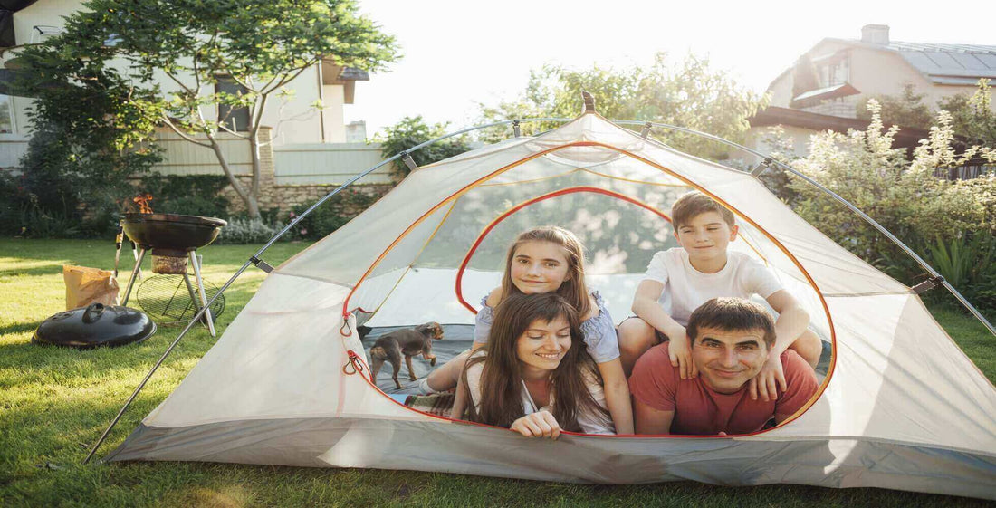 Family enjoying backyard camping in a tent on a sunny day, with a grill nearby for cooking outdoor meals.