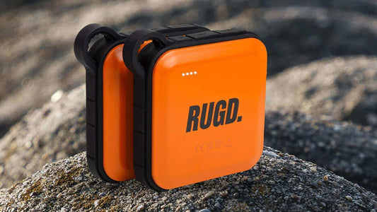 Rugged orange power bank for camping sits on a rocky surface, ideal for keeping devices charged on outdoor adventures.