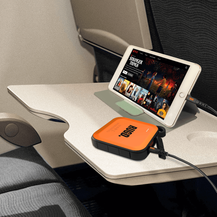 Portable charger connected to a tablet on an airplane tray table for safe charging and device longevity.