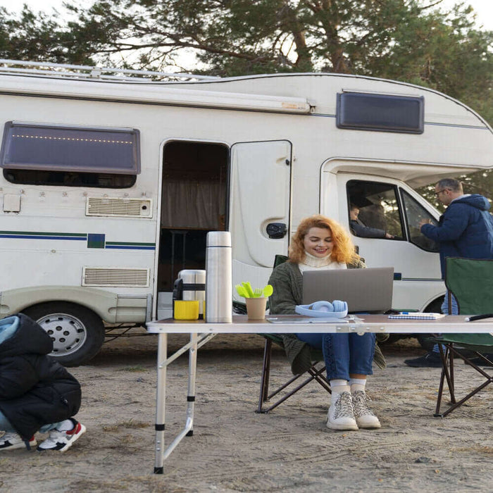 Family enjoying full-time RV living, working at a laptop, and camping near their motorhome in a scenic forest area.