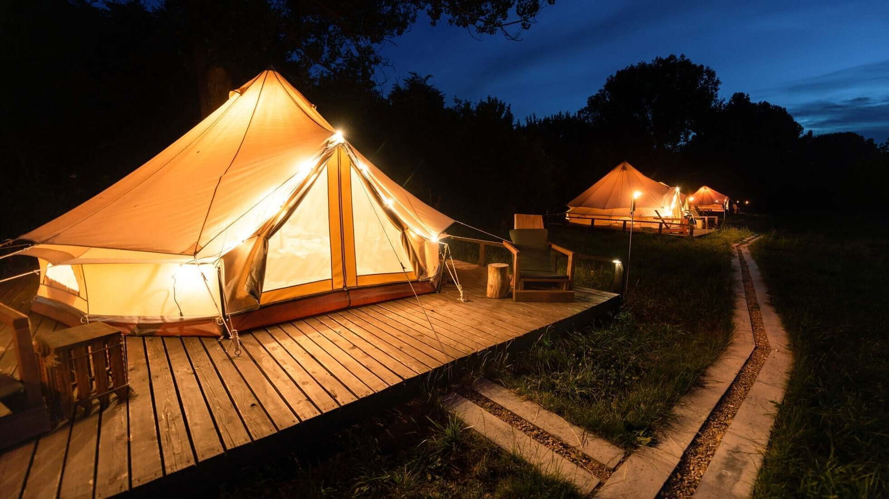 Luxury glamping tents illuminated at night in a scenic UK campsite, offering a blend of comfort and nature