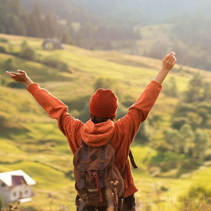 Traveler in red jacket embracing nature on slow travel journey, overlooking scenic green valley and mountains.