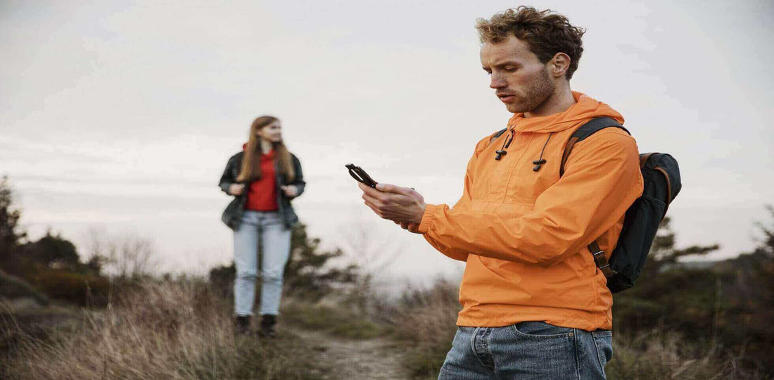 Camper using a smartphone app for navigation during a hike in the wilderness with a companion in the background.