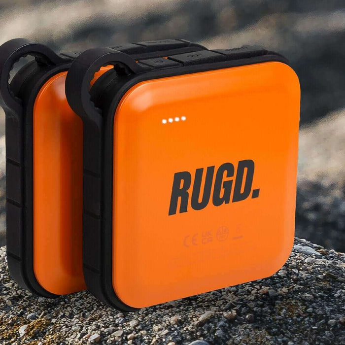 Rugged orange power bank for camping sits on a rocky surface, ideal for keeping devices charged on outdoor adventures.