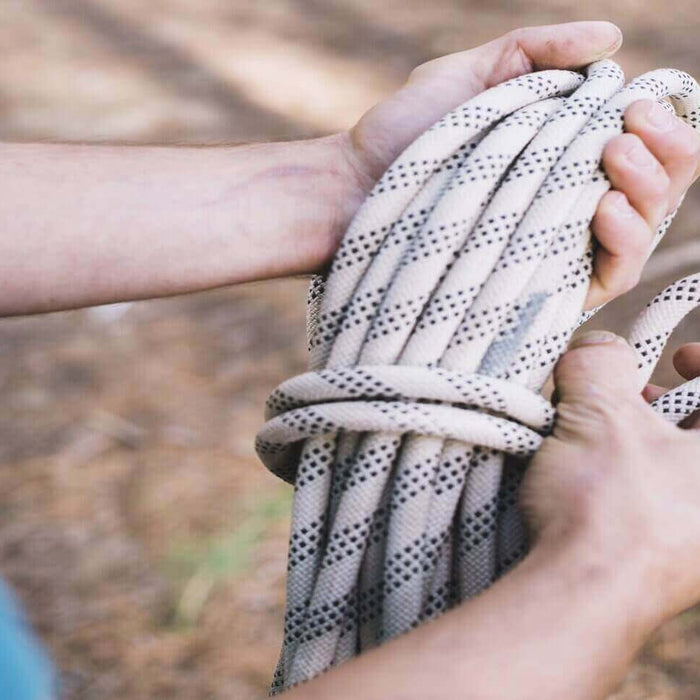 Person demonstrating how to tie an essential camping knot with a rope in a forest setting.