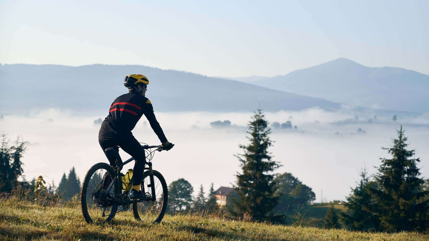 Cyclist wearing essential biking gear rides a mountain bike in scenic landscape with fog and mountains in the background