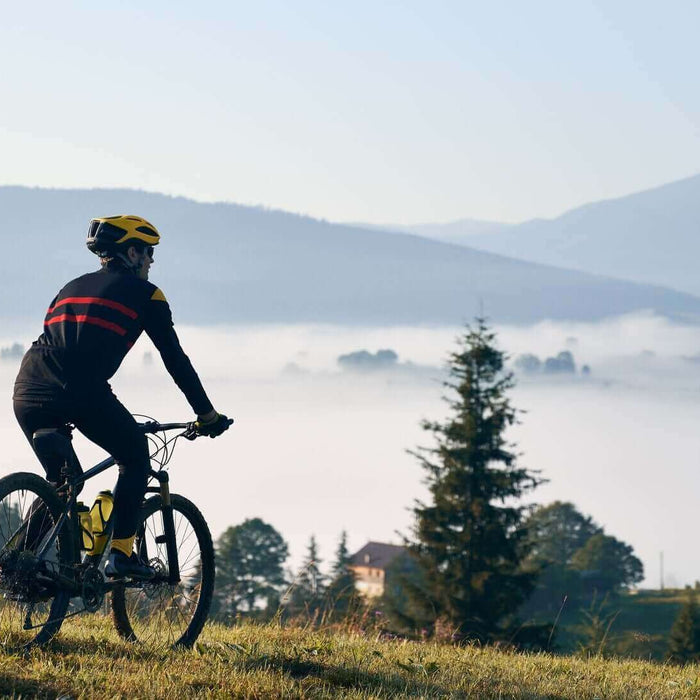 Cyclist wearing essential biking gear rides a mountain bike in scenic landscape with fog and mountains in the background