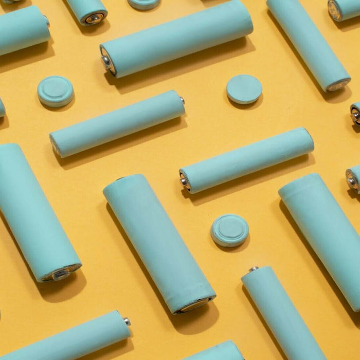 Various sizes of blue cylindrical batteries on a yellow background representing different battery technologies.