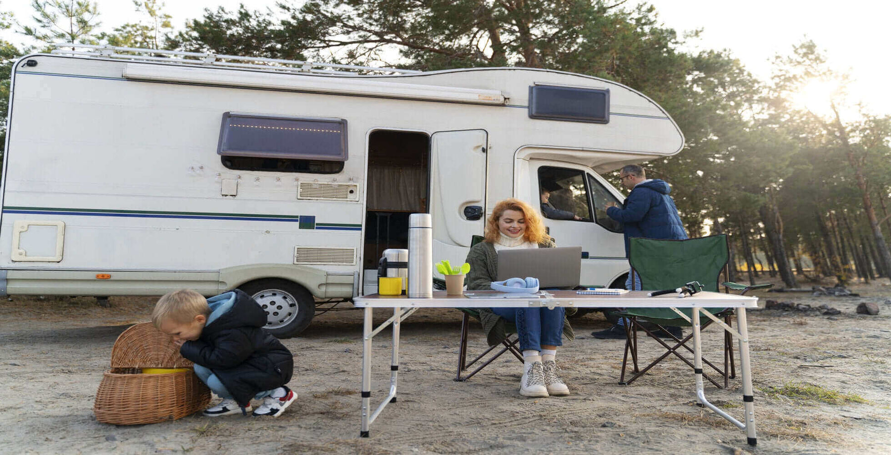 Family enjoying full-time RV living, working at a laptop, and camping near their motorhome in a scenic forest area.