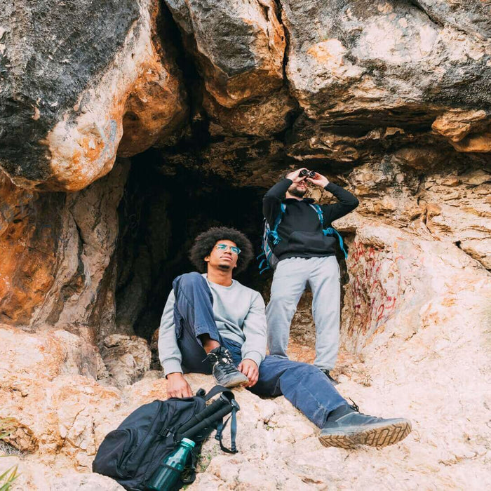 Two cavers resting outside a rocky cave entrance on a caving trip in the UK.