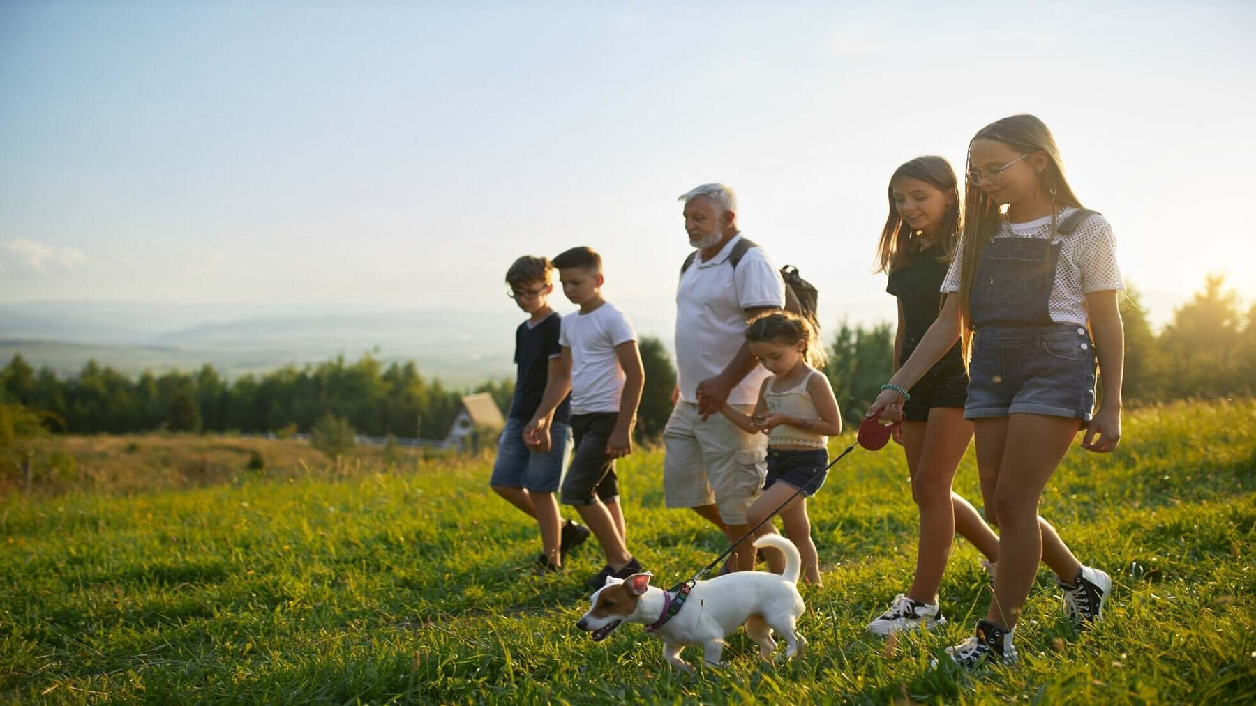 Family hiking with their dog in a grassy field during sunset