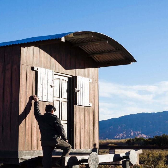 Man entering an off-grid cabin in a remote location with mountain views, showcasing sustainable living and independent lifestyle.