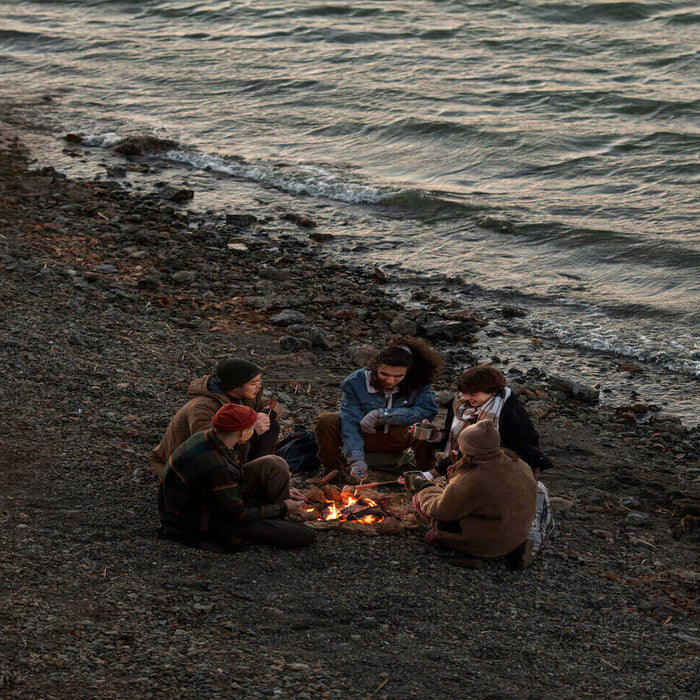 Group of friends enjoying a beach campfire near the ocean, illustrating the essentials for a perfect coastal camping adventure.