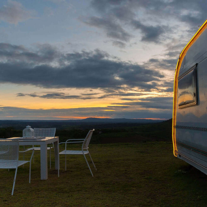 Utility trailer camping setup with table and chairs at sunset in a scenic outdoor location.