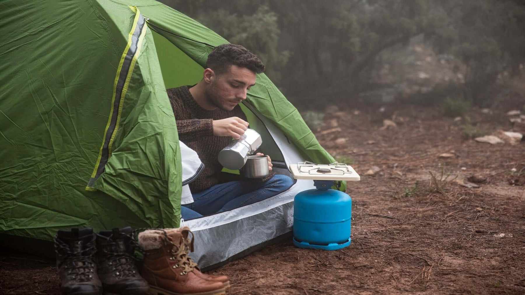 Solo camper pouring drink next to green tent and camping stove in the UK wilderness